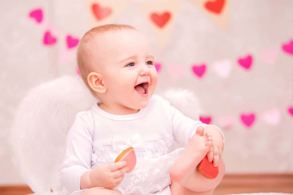 Portrait of a cheerful little girl with white feather wings eating heart-shaped cookies, a symbol of Valentine's Day