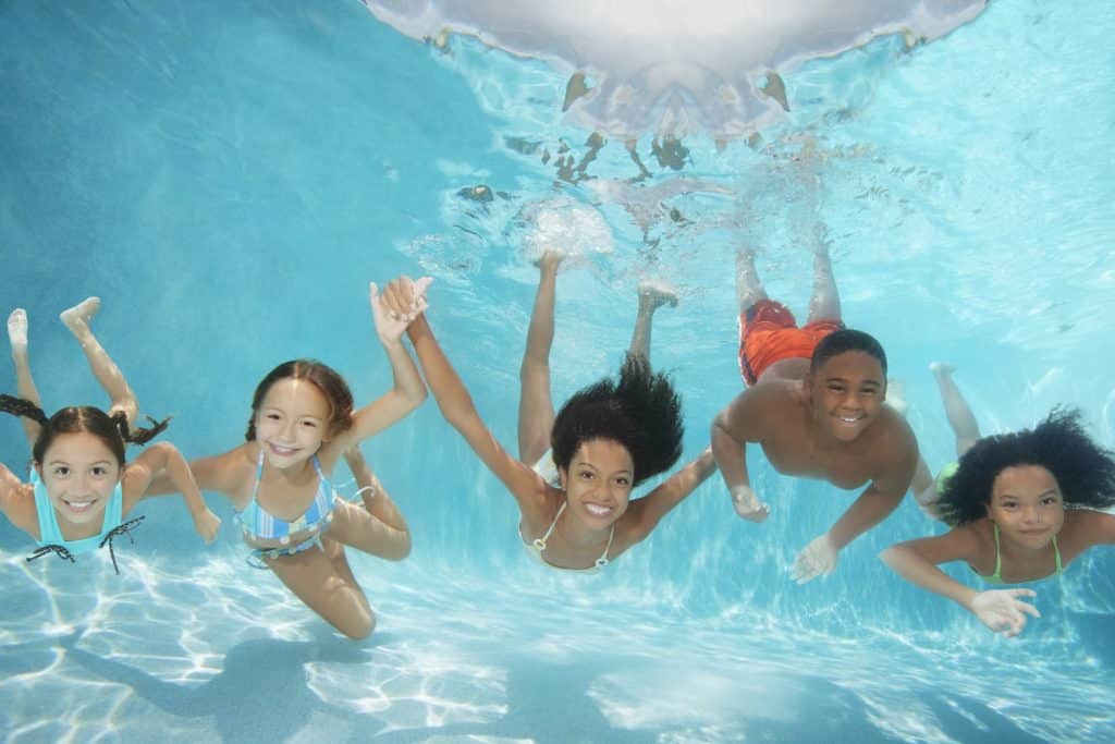 Children (6-13) swimming underwater in pool, smiling