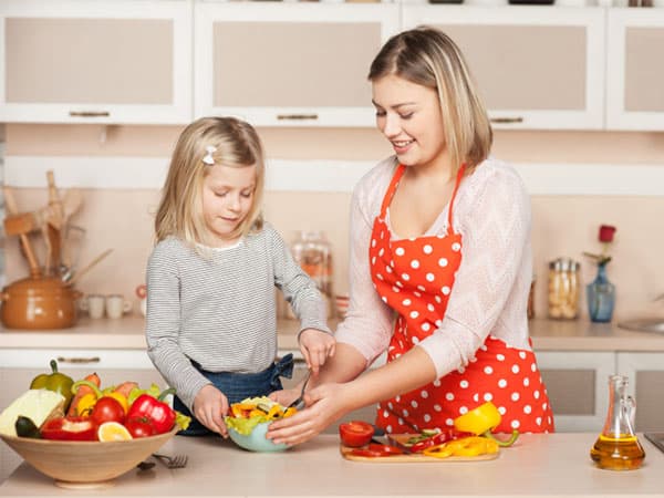 Smiling young mother and her little daughter cooking salad