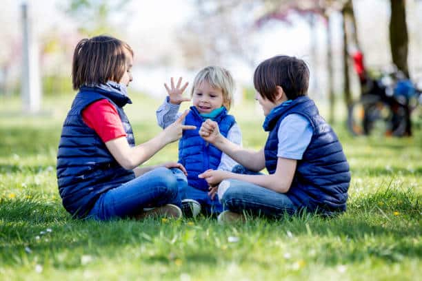 Three children, boy brothers, playing rock scissors paper game in blooming park