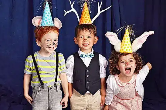 Three children wearing party hats and smiling for the camera at the Animal Antics celebration