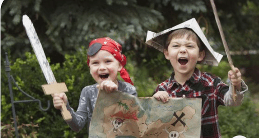 Two children excitedly hold up a map and a pirate hat during an Art Treasure Hunt