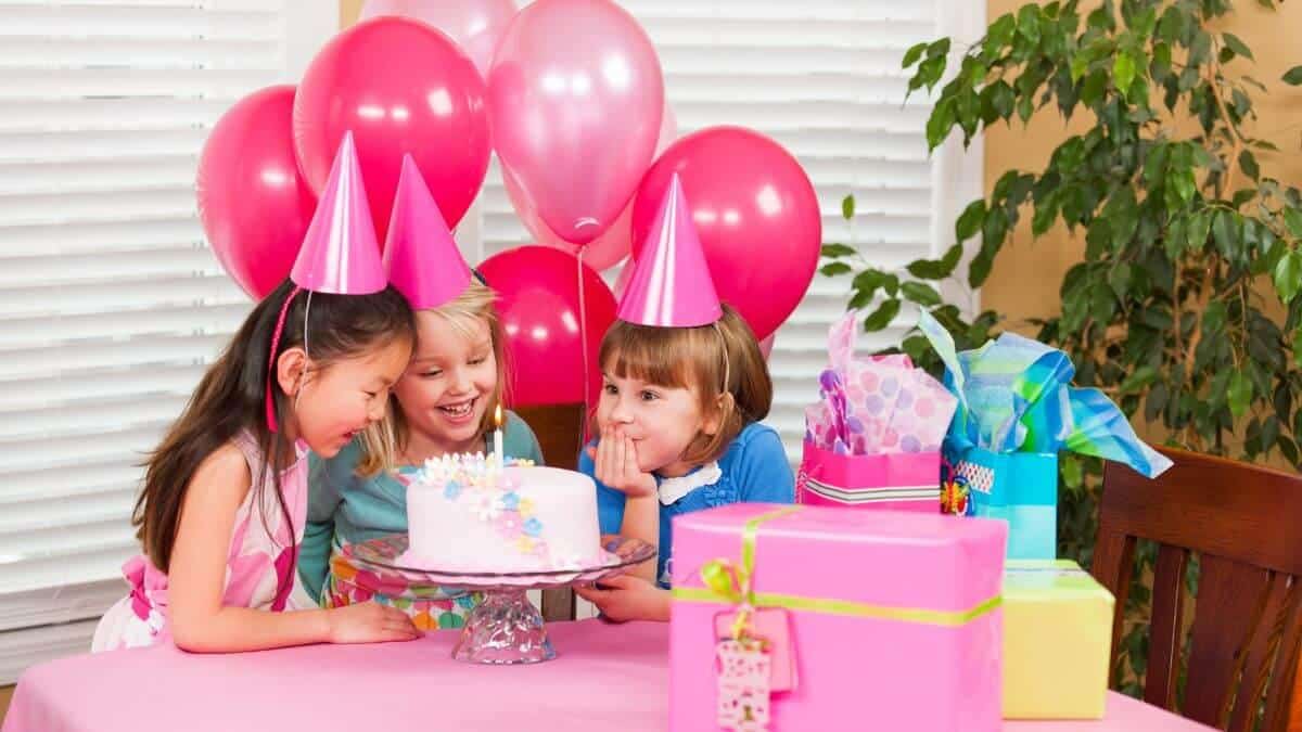 Three children sitting at a table with a birthday cake, celebrating at one of the best party places for five-year-olds.