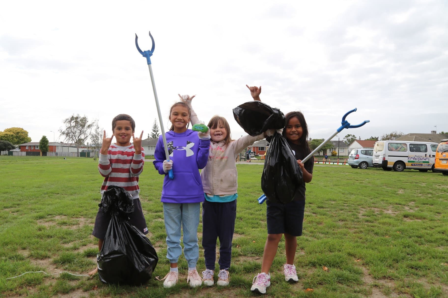 Four children holding up shovels and a blue rake at a Community Cleanup Event