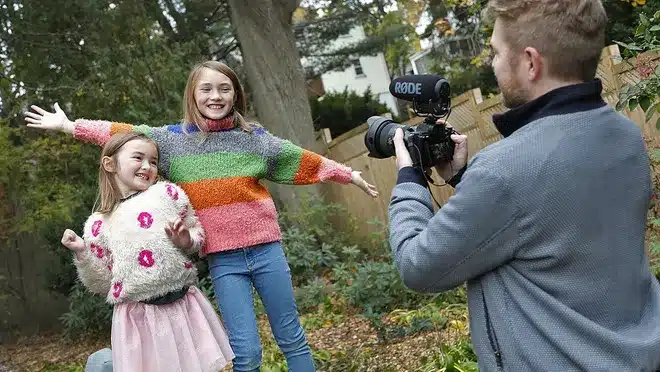 A man capturing a moment as he photographs two girls in a yard, while working on creating a short film