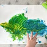 A child's hands painting a green and blue fish. Learn how to create a mess-free finger painting space at home