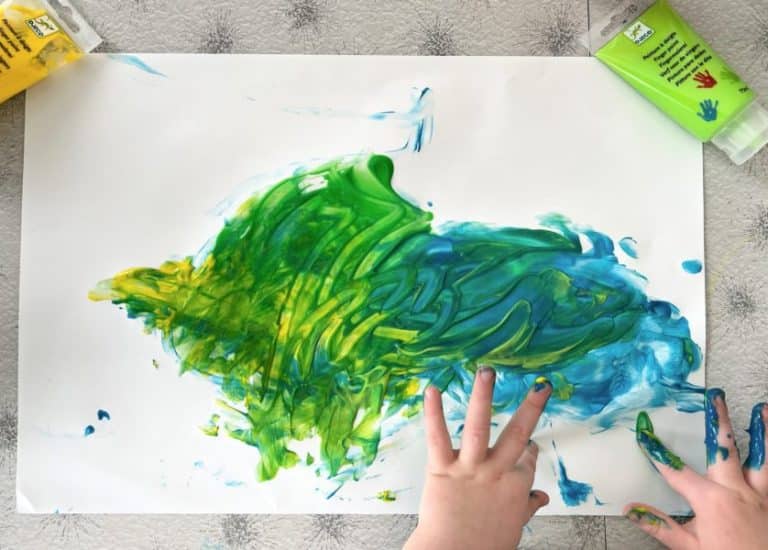 A child's hands painting a green and blue fish. Learn how to create a mess-free finger painting space at home