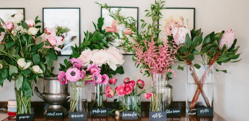 A table with vases of flowers and signs at an Interactive Flower Bar