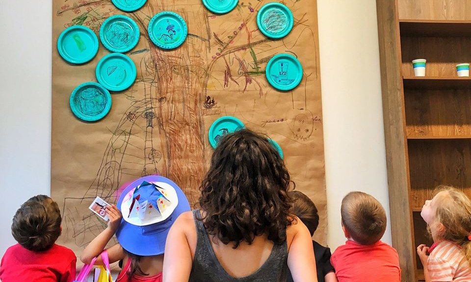 A woman and children at an Interactive Workshop, looking at a paper plate tree.