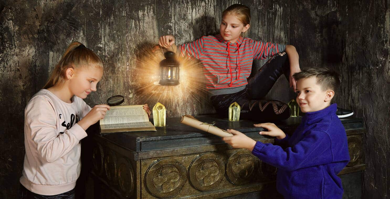 Three children examining a table with a lamp and a book. A potential scene from an Escape Room for Kids