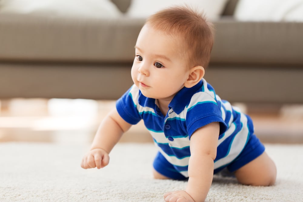 A baby exploring the floor in front of a couch during the crawling stage, typically occurring between months 7-9.
