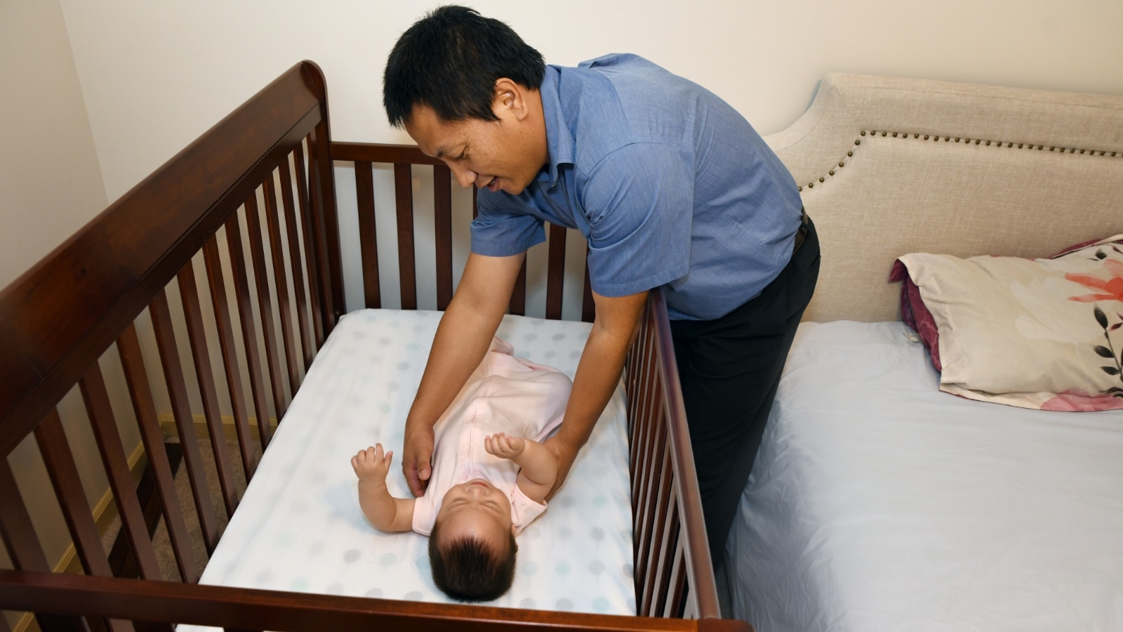 A caring man assists a baby in a crib, ensuring a safe sleeping environment for the little one