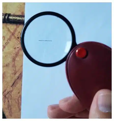 A person using a magnifying glass to examine a piece of paper with super-tiny text.
