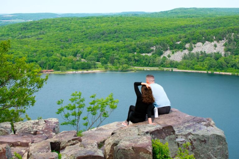 A couple enjoying a serene view of a lake while sitting on a rock. Experience the hidden gems of Wisconsin's outdoor adventures