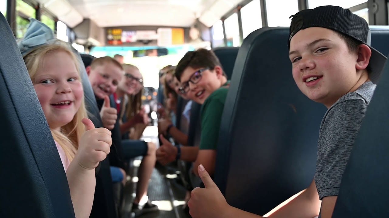 Children on a school bus, happily giving thumbs up, ready for their field trip adventure