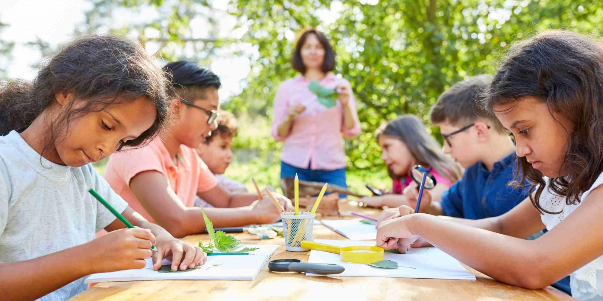 Children at a table drawing with pencils - an engaging outdoor learning activity fostering creativity and artistic expression
