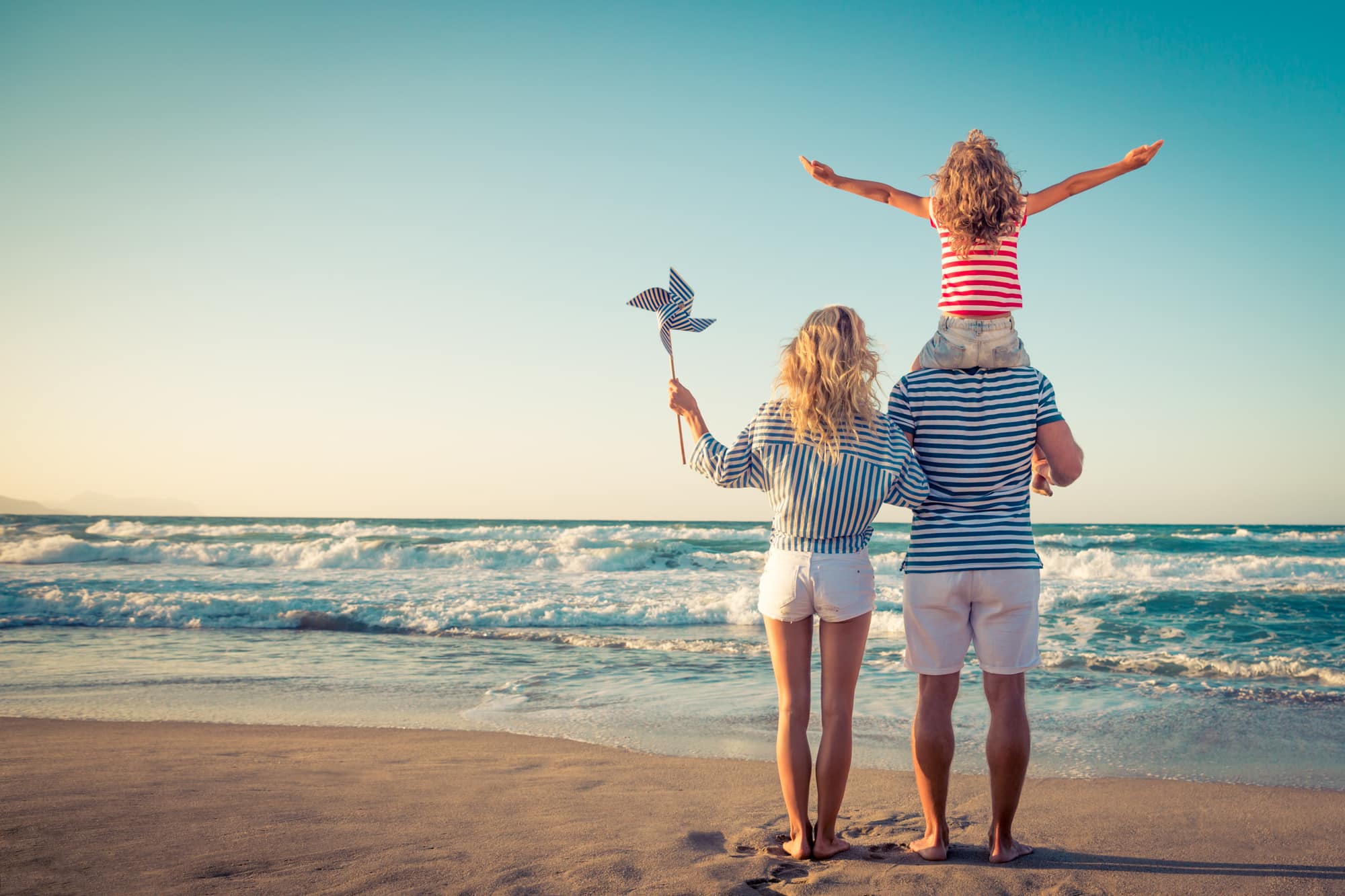A joyful family on the beach, arms raised in celebration, enjoying a budget-friendly holiday together.