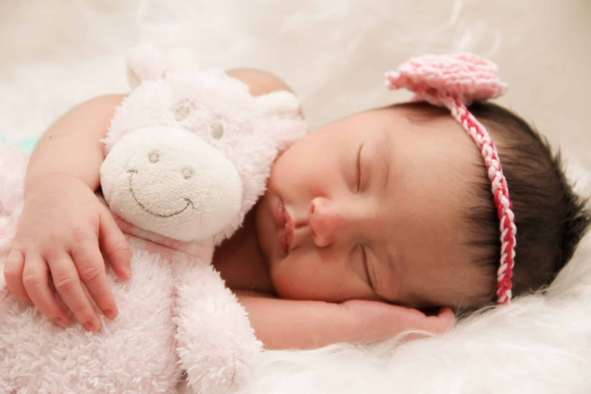A baby peacefully sleeping with a stuffed animal.