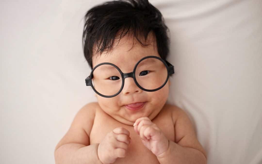 A baby with glasses laying on a bed