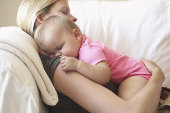 A woman cradling a baby on a couch.